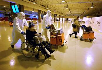 Trabajadores con máscaras y trajes protectores ayudan a salir a viajeros procedentes de China en el aeropuerto de Fiumicino, Roma.
