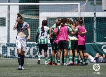 Sanadri se lamenta en primer plano mientras las jugadoras béticas celebran la permanencia al final del partido.