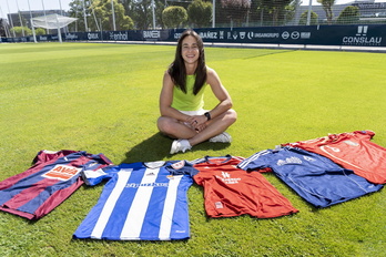 La ya ex futbolista del Osasuna Leyre Fernandez posando sonriente junto a las camisetas de los equipos en los que ha jugado.