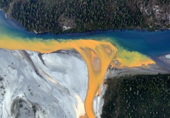 Vista aérea del río Kutuk en el Parque Nacional Puertas del Ártico de Alaska en la que se aprecia el color naranja extendiéndose en el agua azul clara.